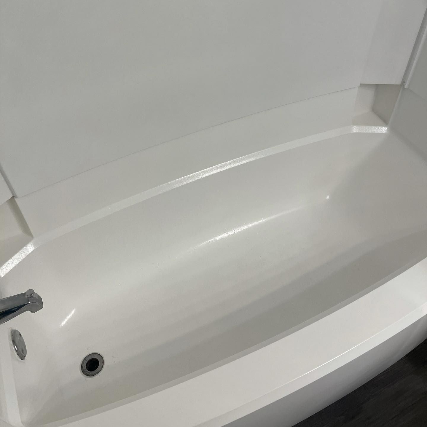 A clean, white bathtub and shower surround with a chrome faucet and drain in a modern bathroom.