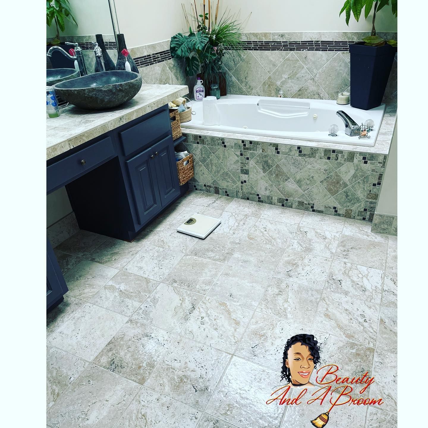 Bathroom with navy vanity, stone vessel sink, tiled tub surround, and light-colored stone floor, featuring a small logo.