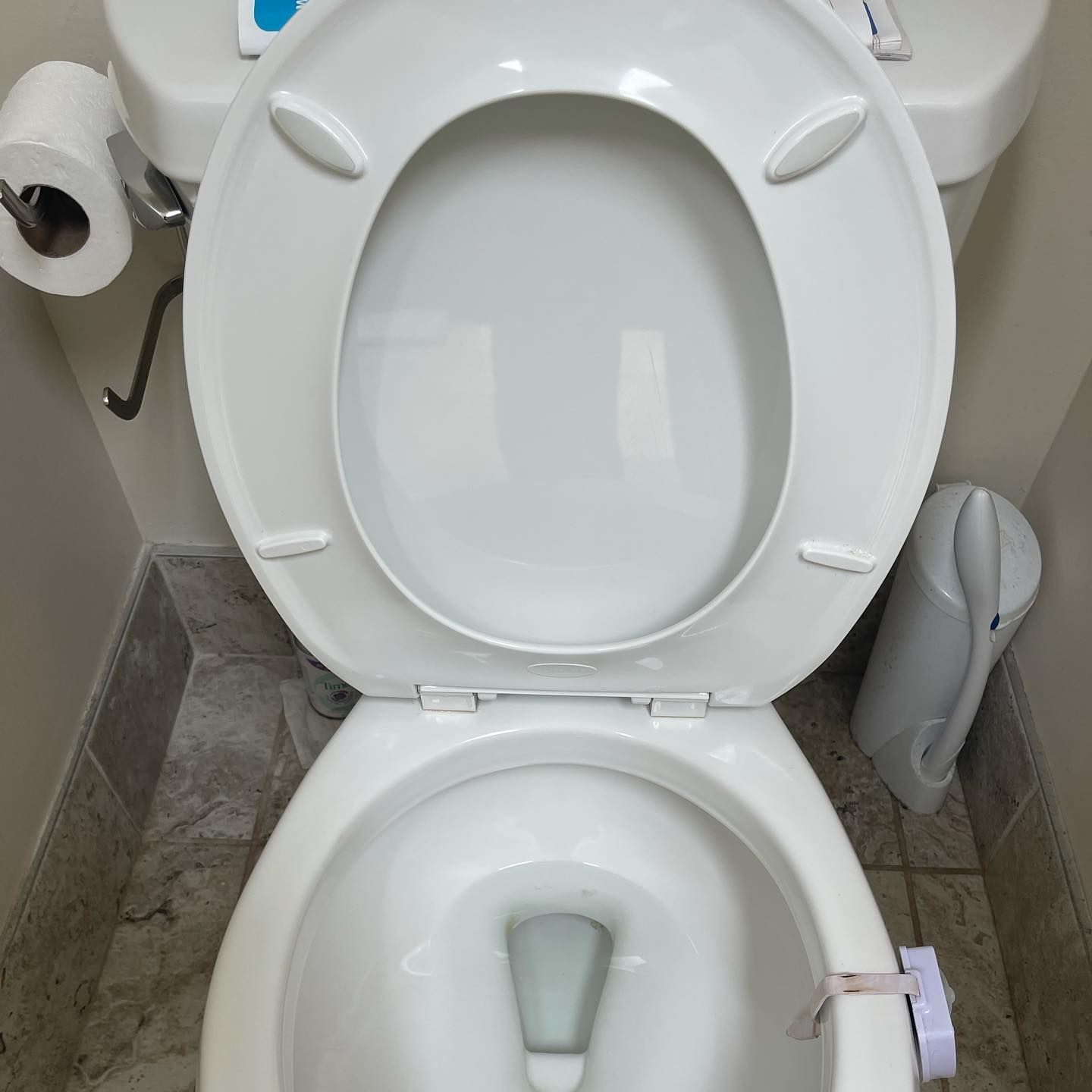 A white toilet with the lid and seat up, showing a small white object attached to the right side of the bowl.