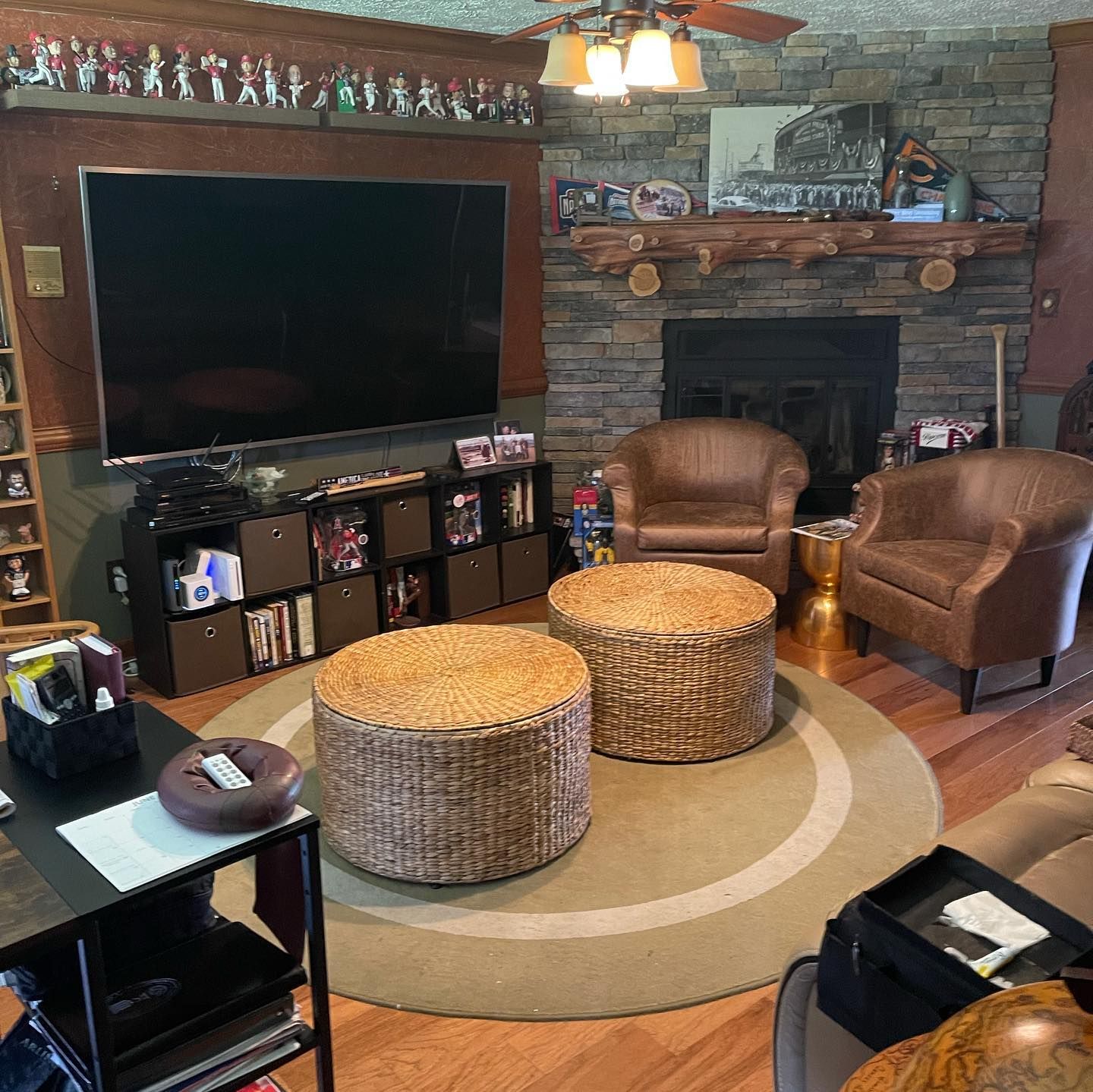 A cozy living room with a stone fireplace, large television on a storage unit, two leather armchairs, and round ottomans.