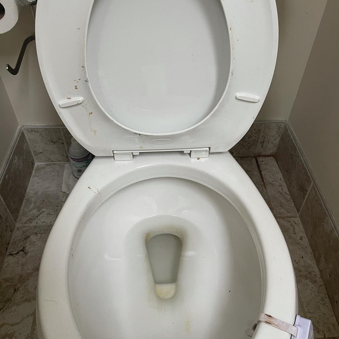 A high-angle view of a white porcelain toilet with the lid and seat raised, positioned on a tiled floor.