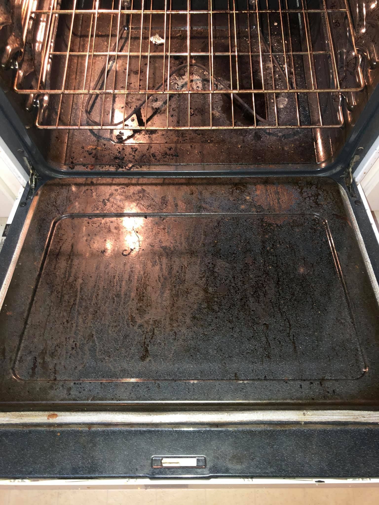 The open door of a dirty kitchen oven showing a dark, grease-stained interior with a metal wire rack inside.