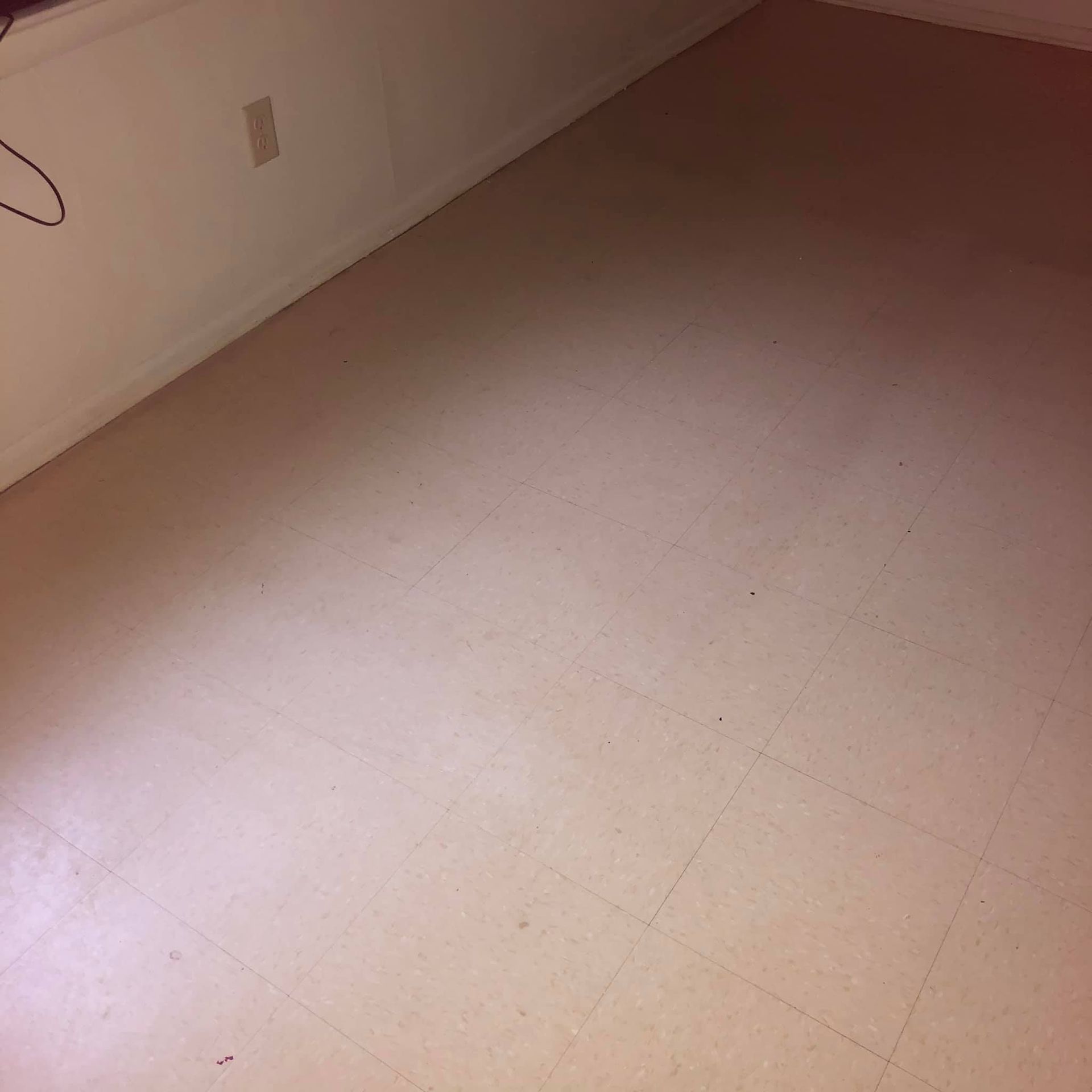 A low-angle view of a beige tiled floor in a corner of a room with white walls and a power outlet.