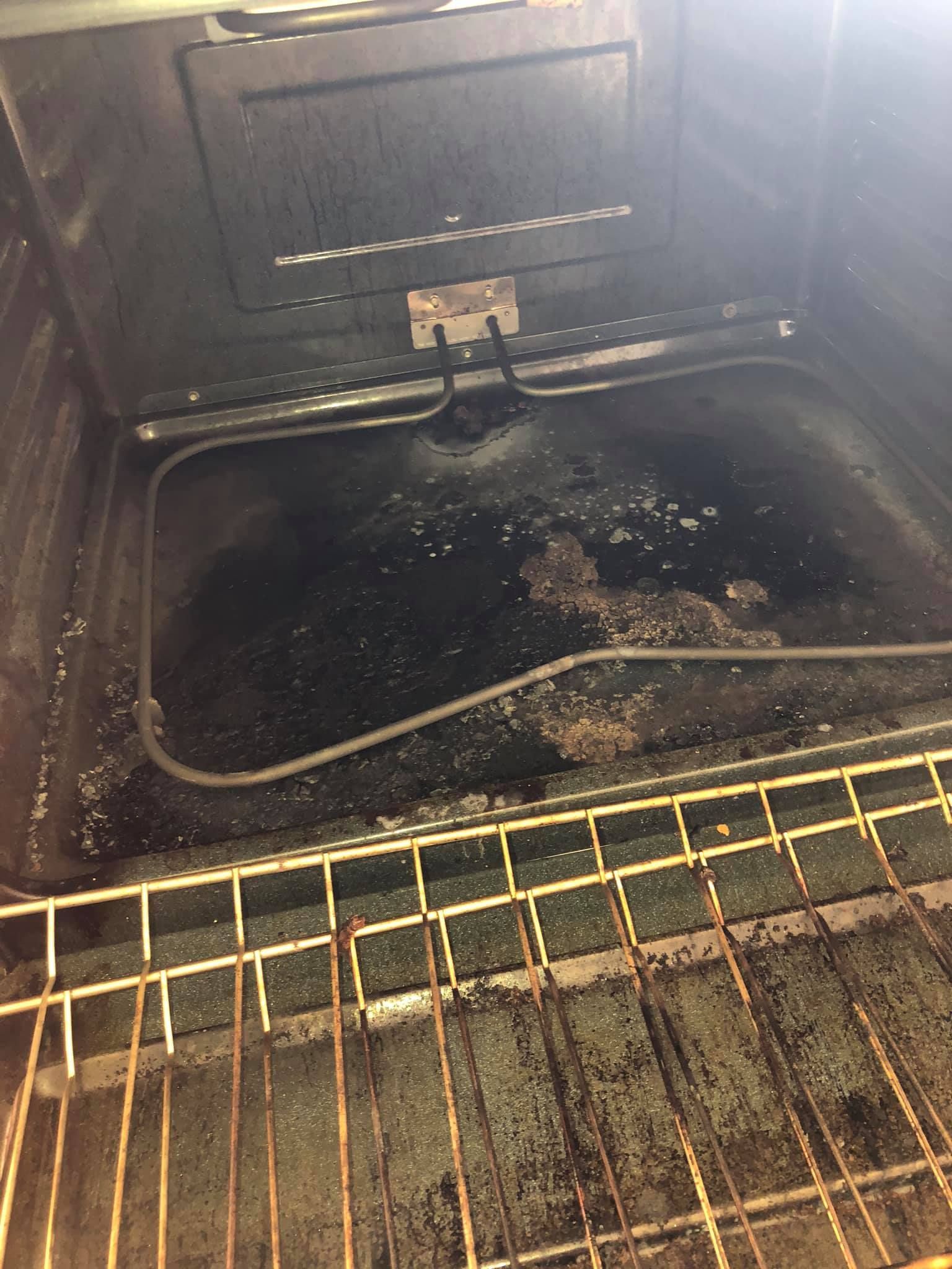 The interior of an oven with a dirty, stained black base and a rusted wire rack in the foreground.