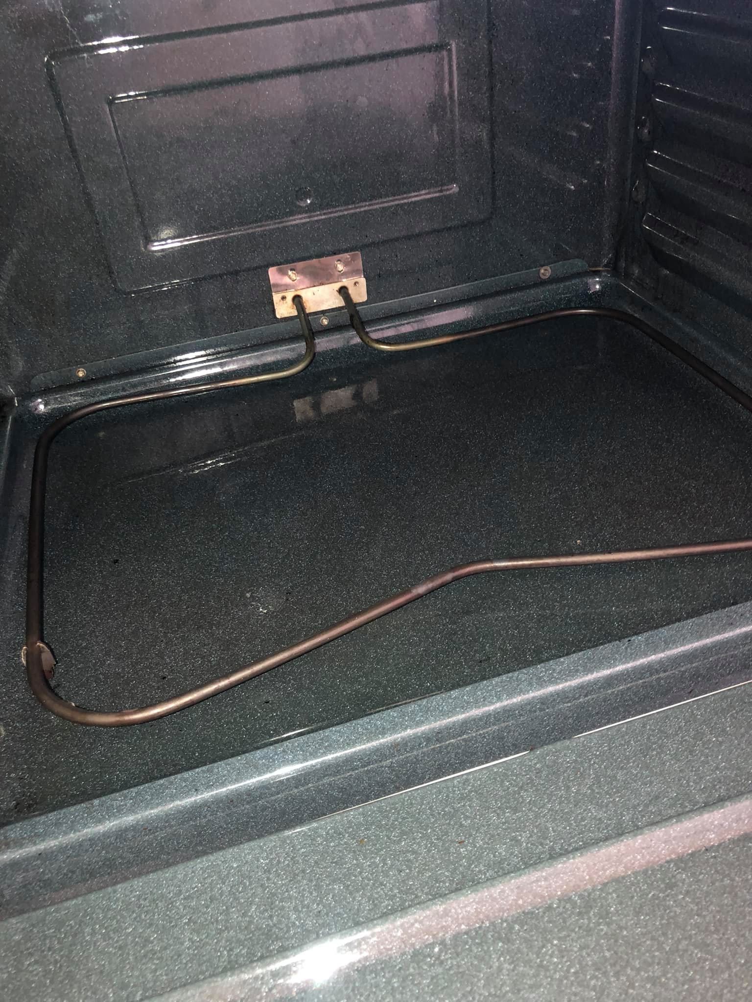 The interior of an oven with a dark, speckled finish and a detached, bent metal heating element lying on the floor.