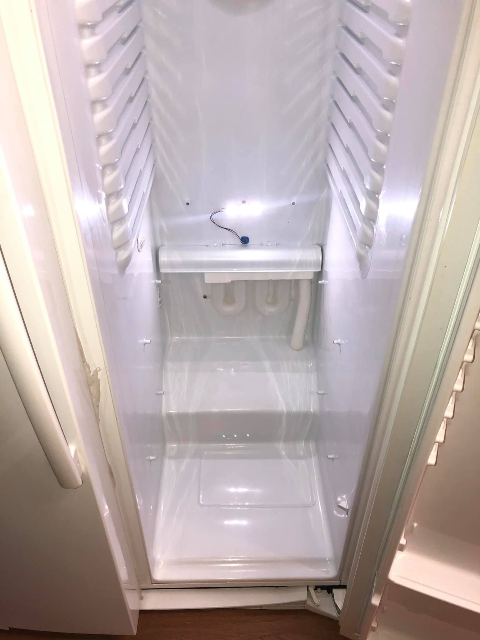Empty, white vertical freezer interior with shelving tracks, a small light, and a lower storage step.