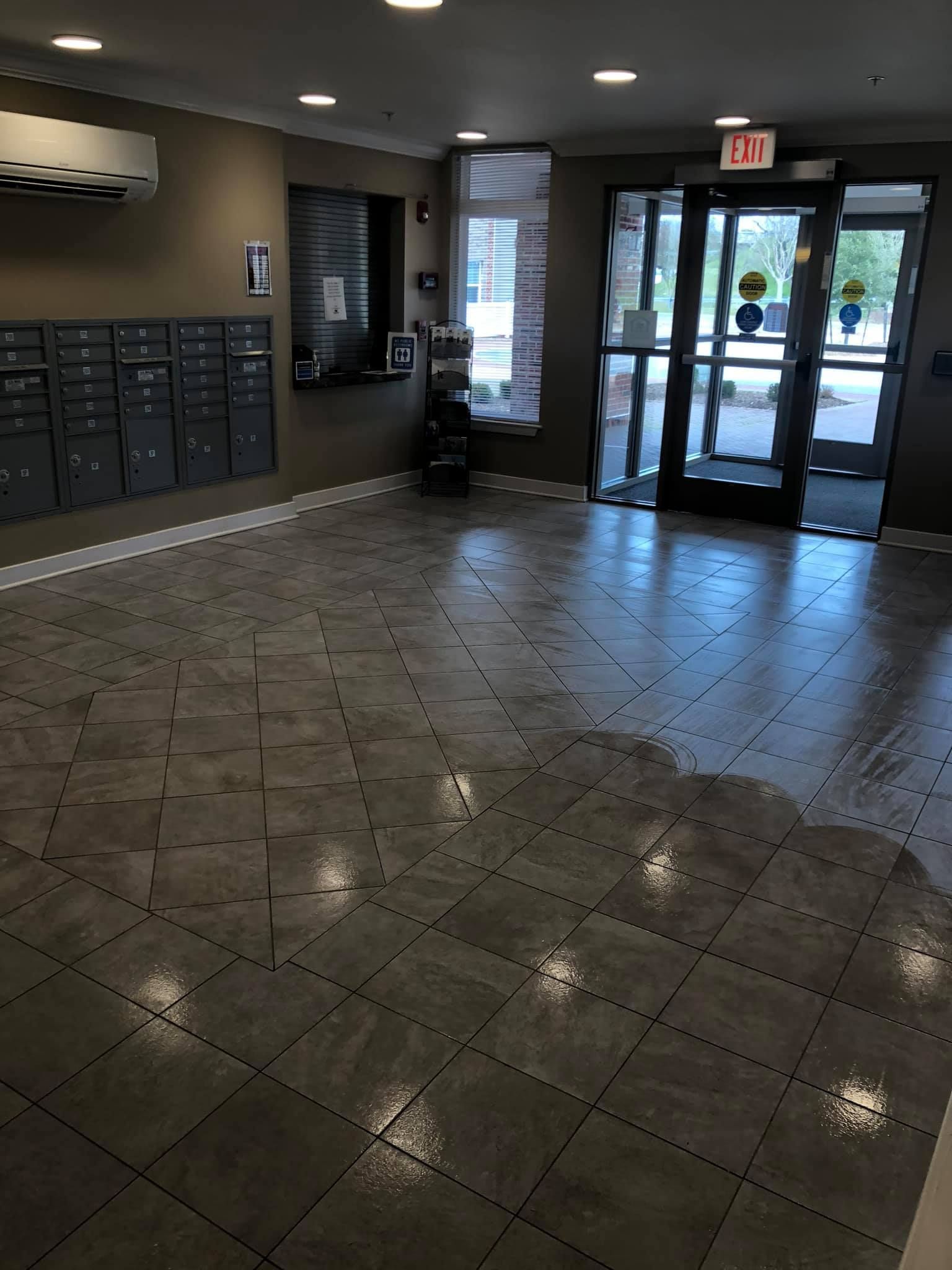 An indoor building lobby with a tiled floor, mailboxes on a wall, and a glass-paneled double door leading outside.