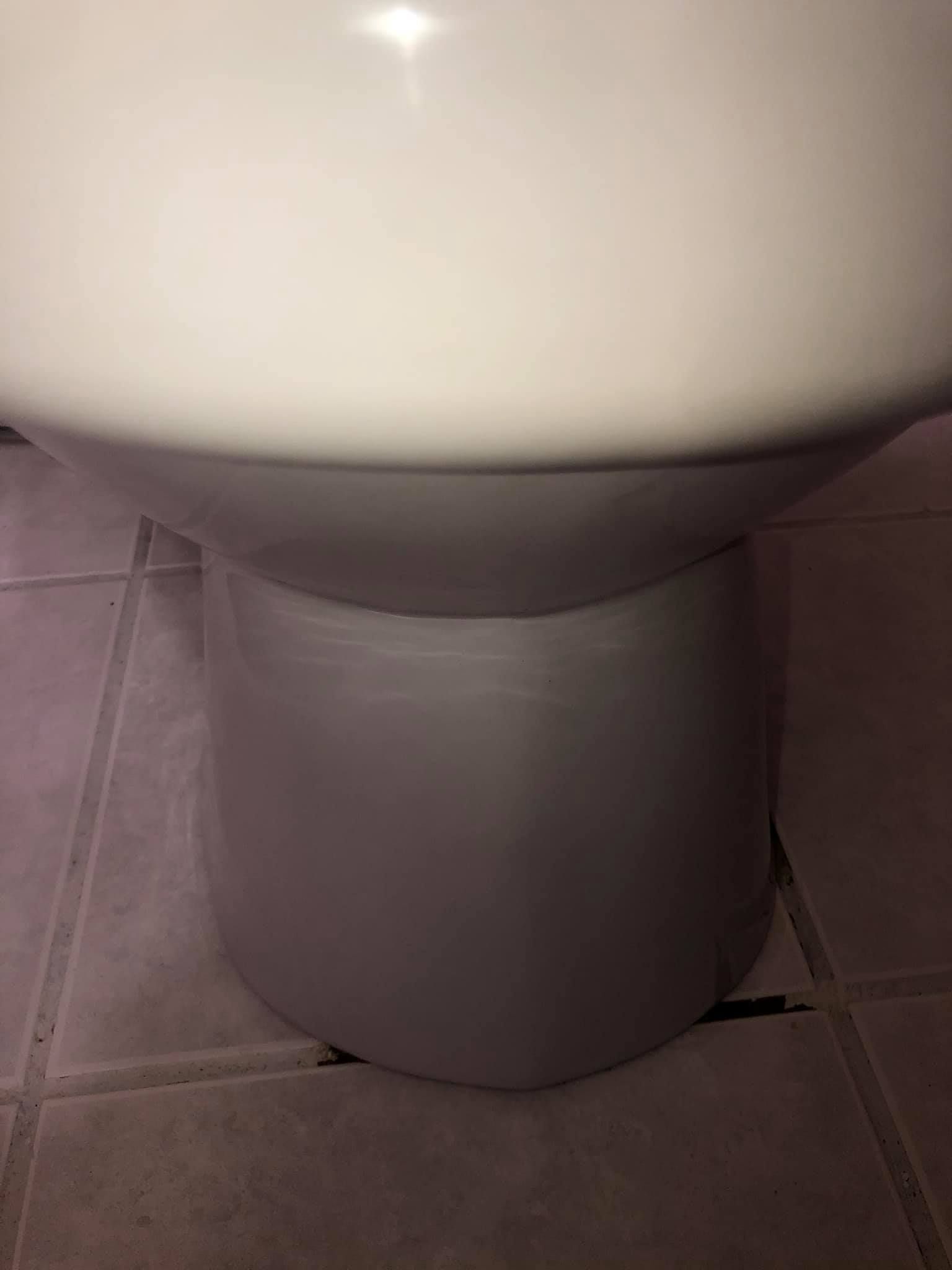A close-up view of the white porcelain base of a toilet sitting on a light-colored tiled floor.