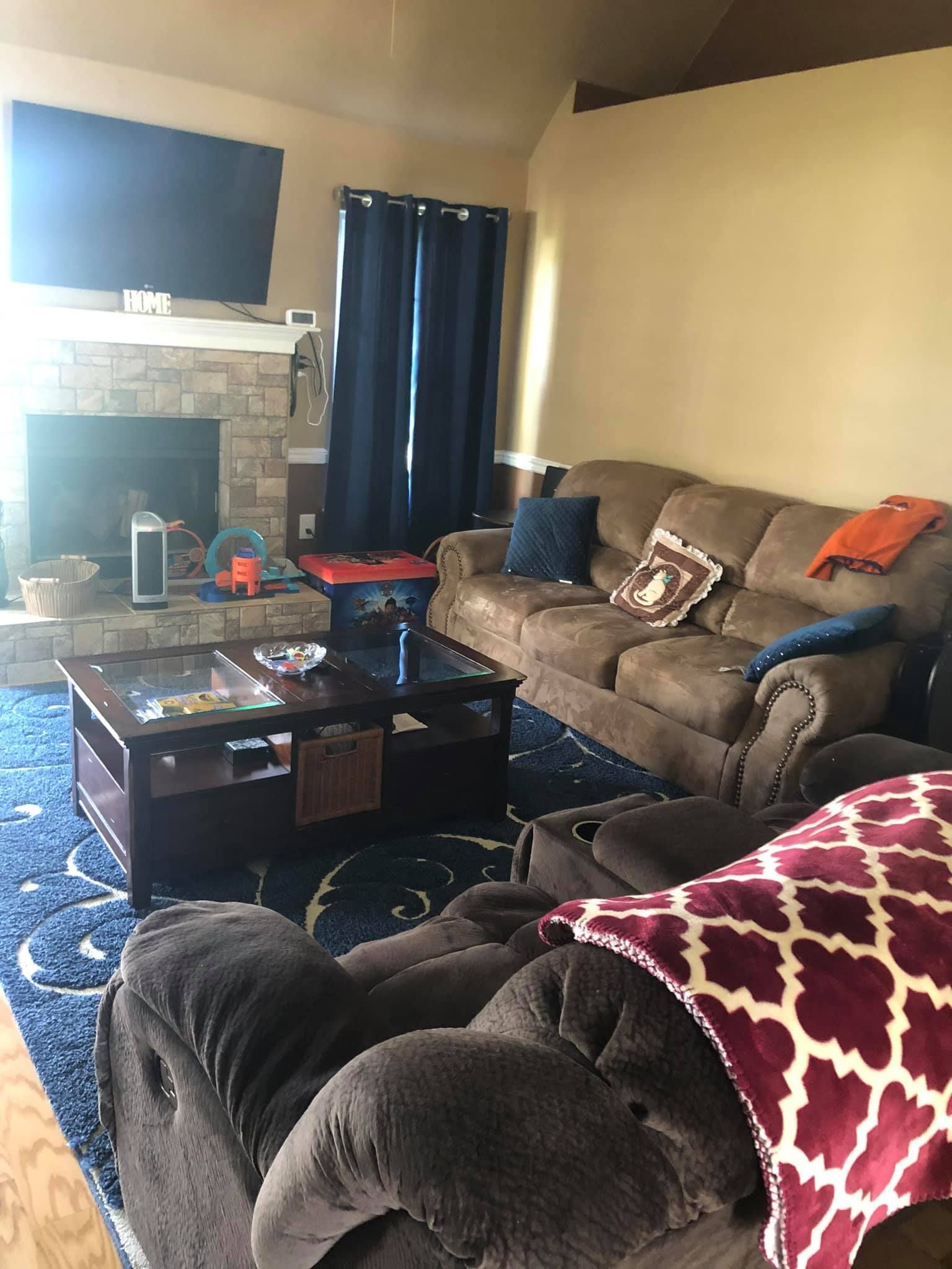 A living room with a fireplace, a television, a brown sofa, and a recliner on a blue patterned area rug.