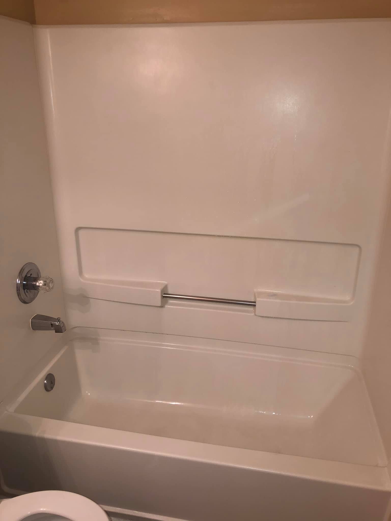 A white fiberglass bathtub and shower surround with a built-in recessed shelf and silver towel bar.
