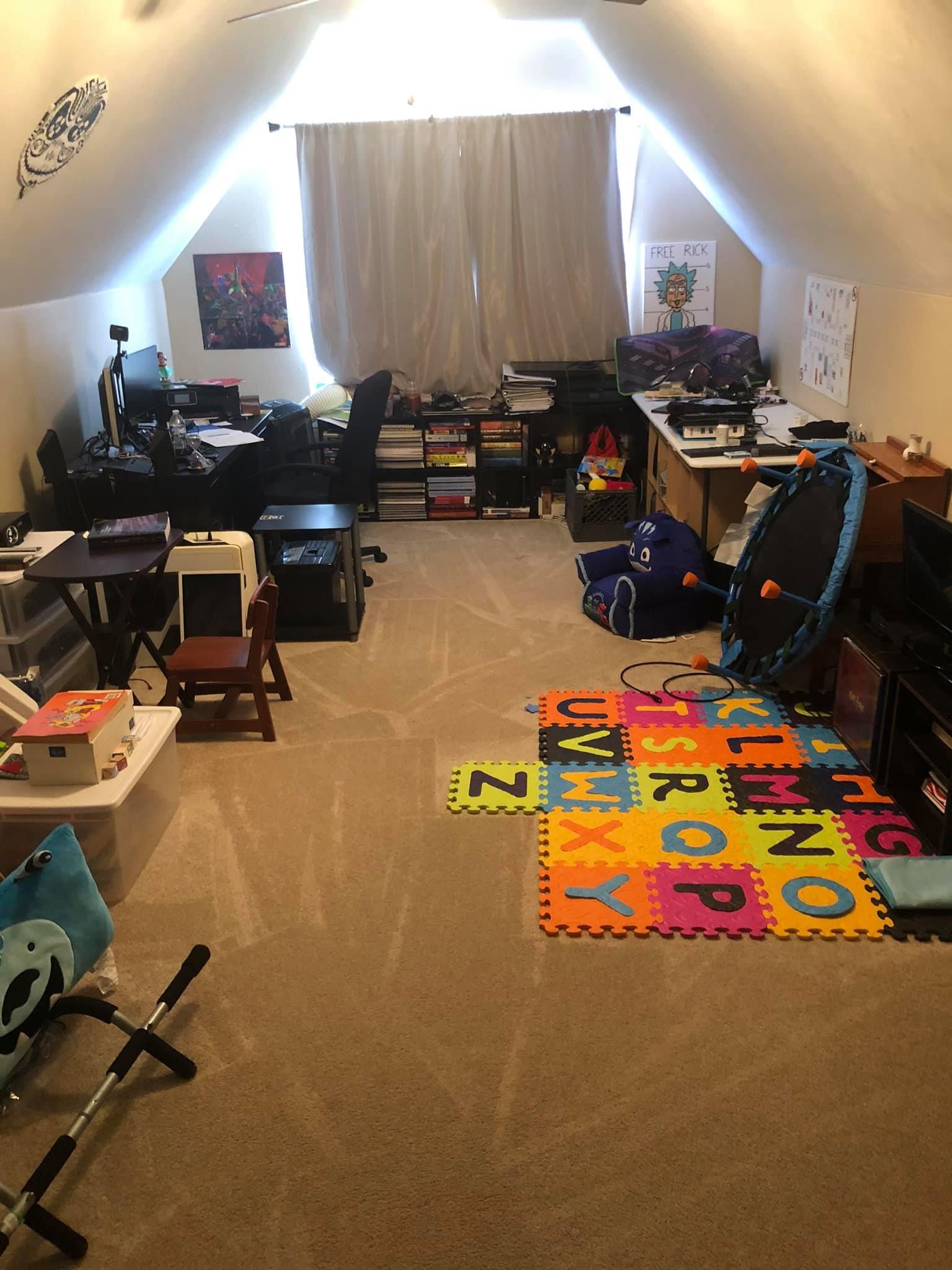 An attic room features a desk setup, a children’s alphabet foam play mat, and various pieces of furniture and equipment.