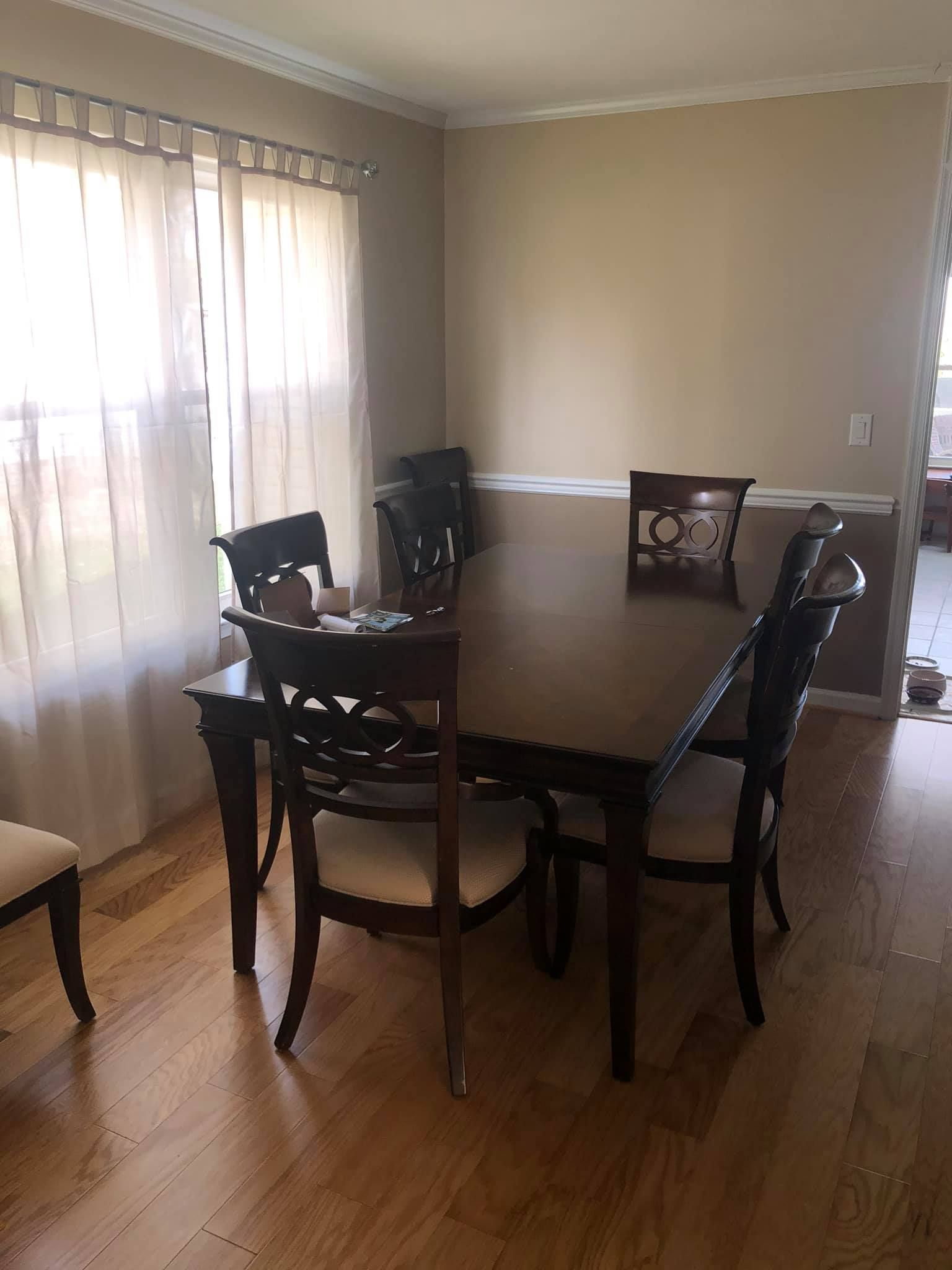 A dining set with a rectangular wooden table and six matching chairs with cream-colored cushions on a hardwood floor.