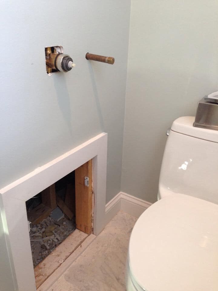 A toilet is sitting in a bathroom next to a hole in the wall.