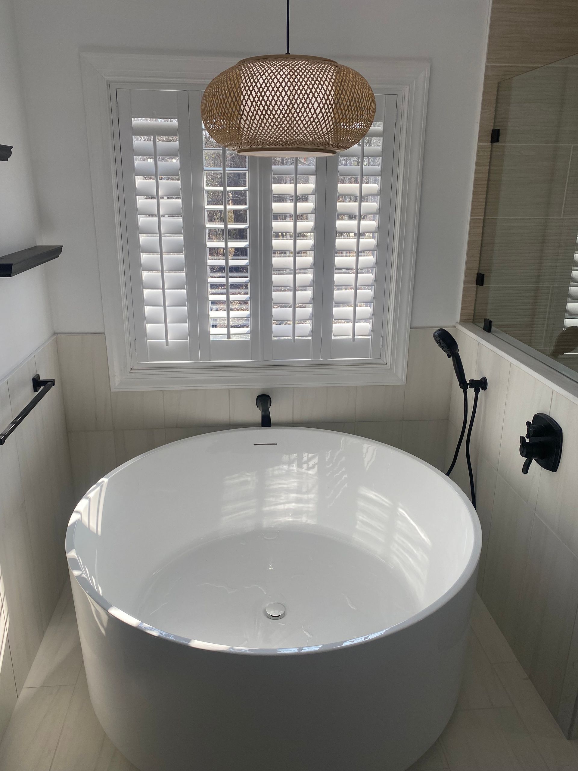 A bathroom with a round bathtub and a window with shutters.