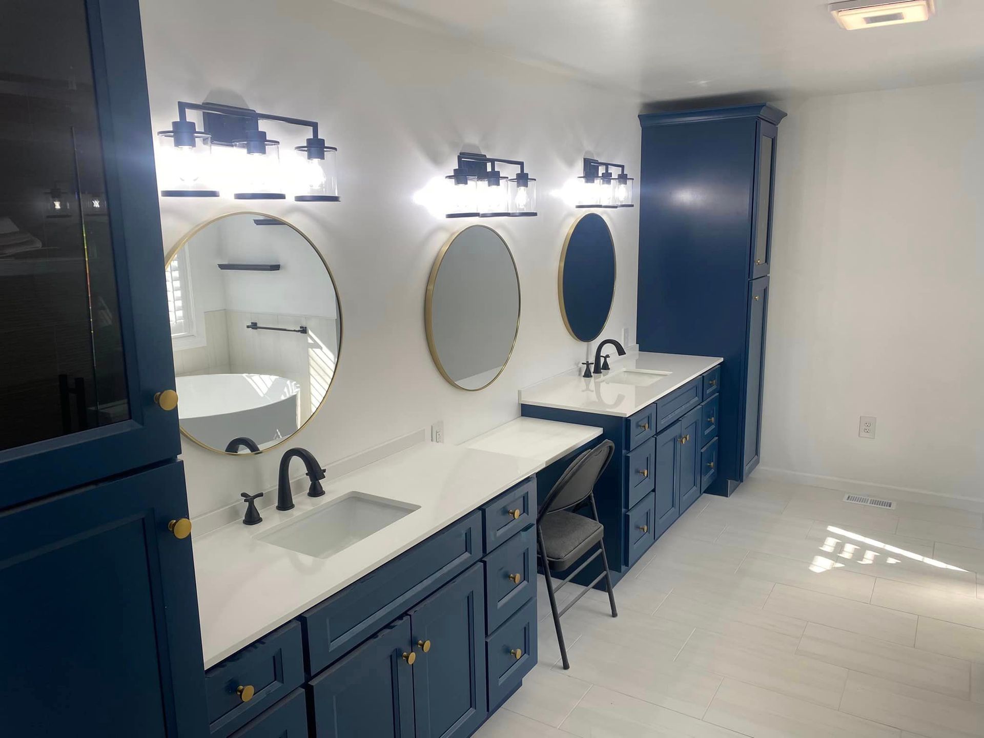 A bathroom with two sinks , two mirrors , and blue cabinets.