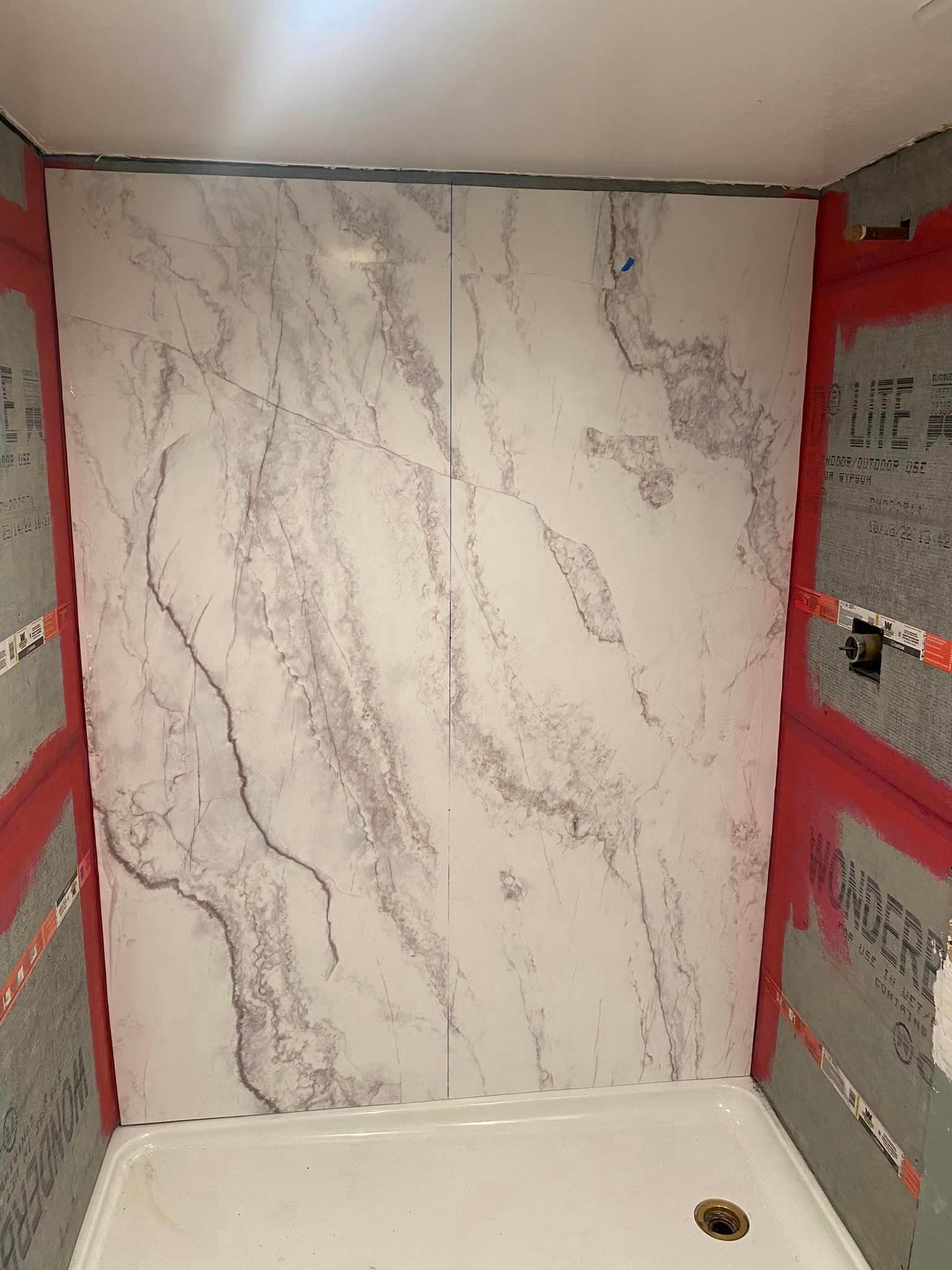 A bathroom with a shower stall and a marble wall.