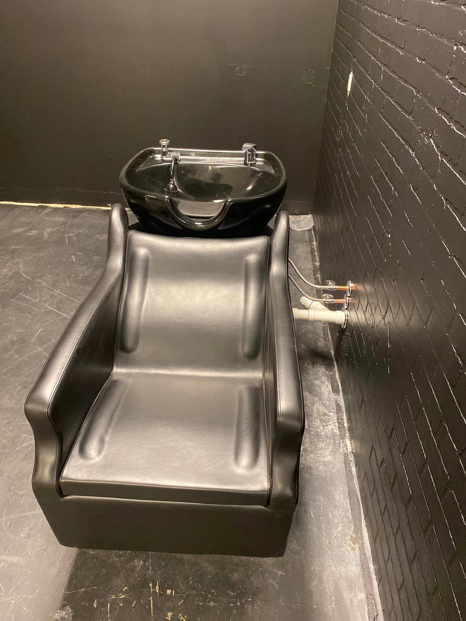 A black shampoo chair is sitting in a room next to a black wall.