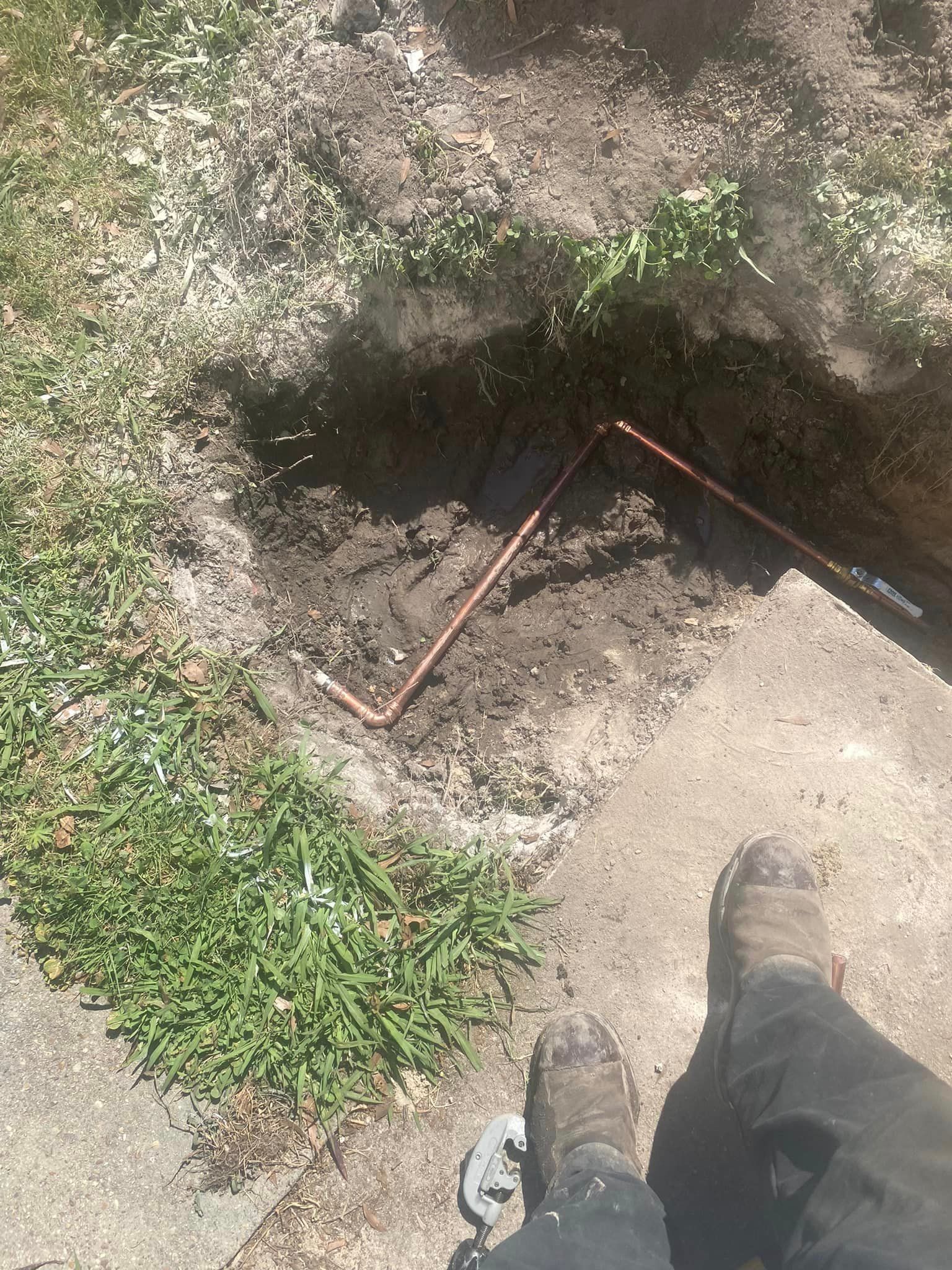 A person is standing on a sidewalk next to a hole in the ground.