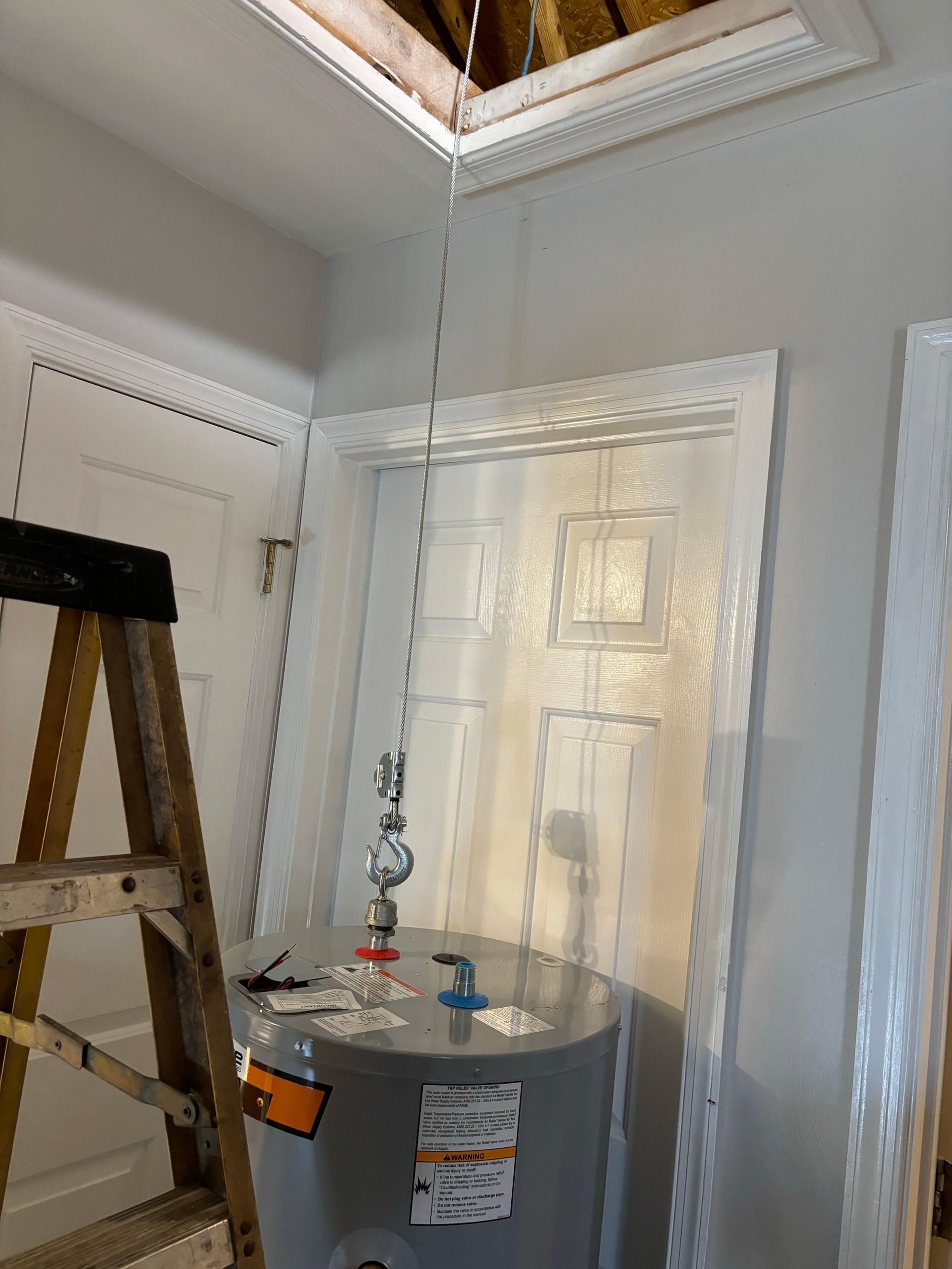 A water heater is sitting in a room next to a ladder.