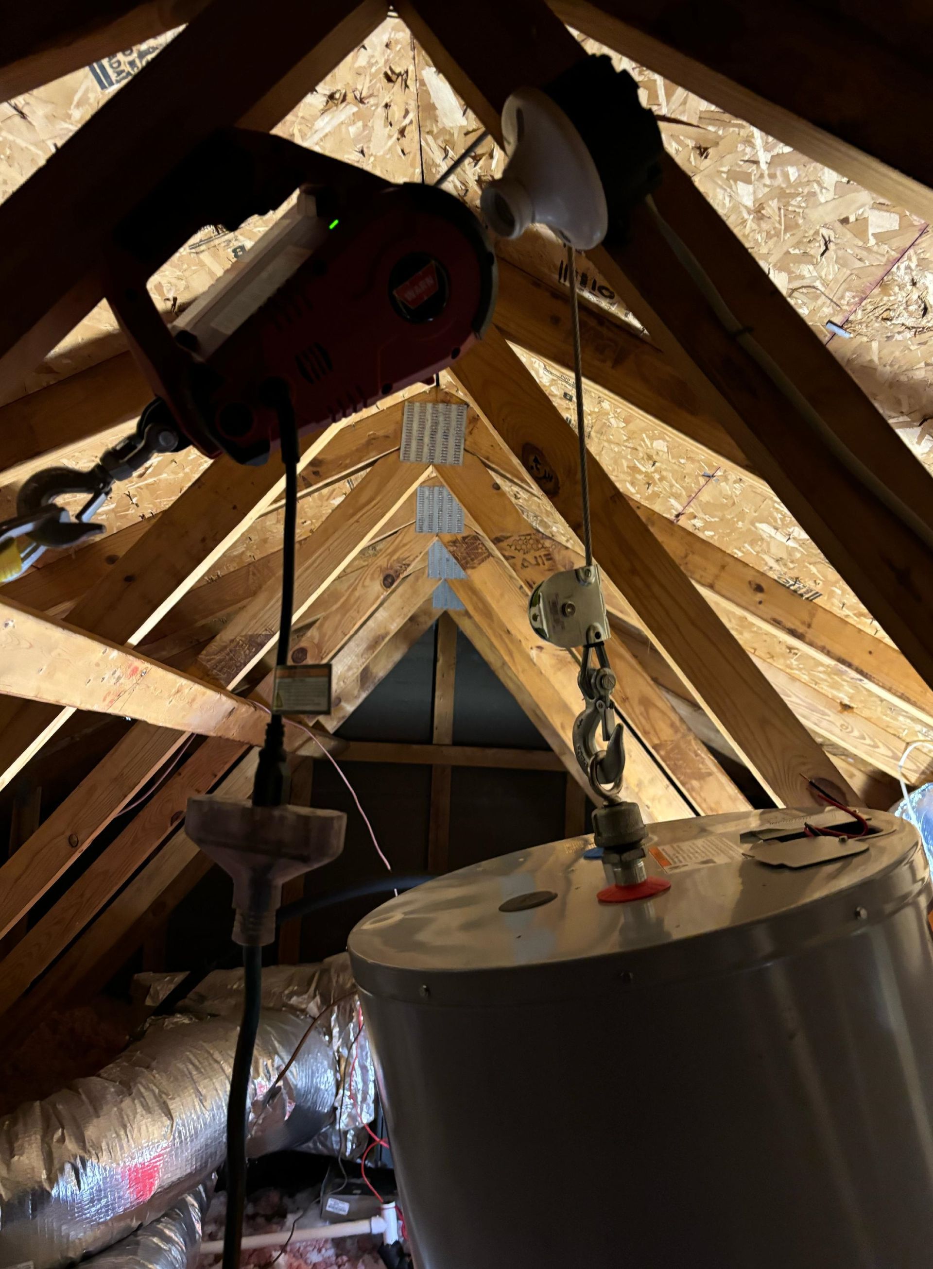 A water heater is hanging from the ceiling of an attic.