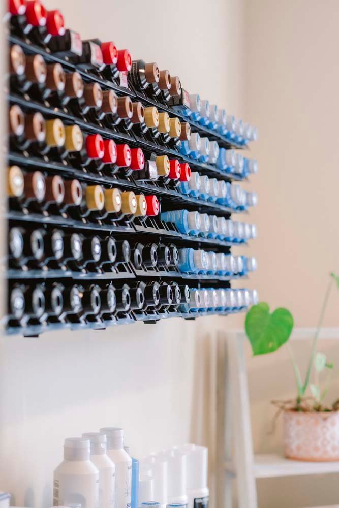 A shelf filled with bottles of nail polish is hanging on a wall.