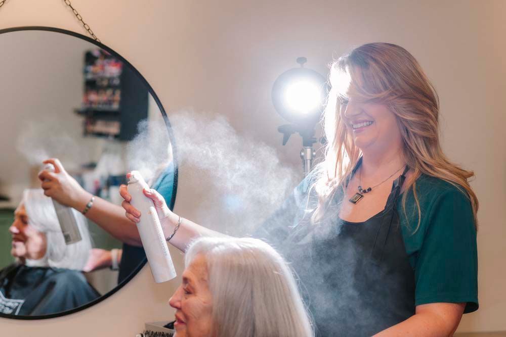 A woman is getting her hair done by a hairdresser in front of a mirror.