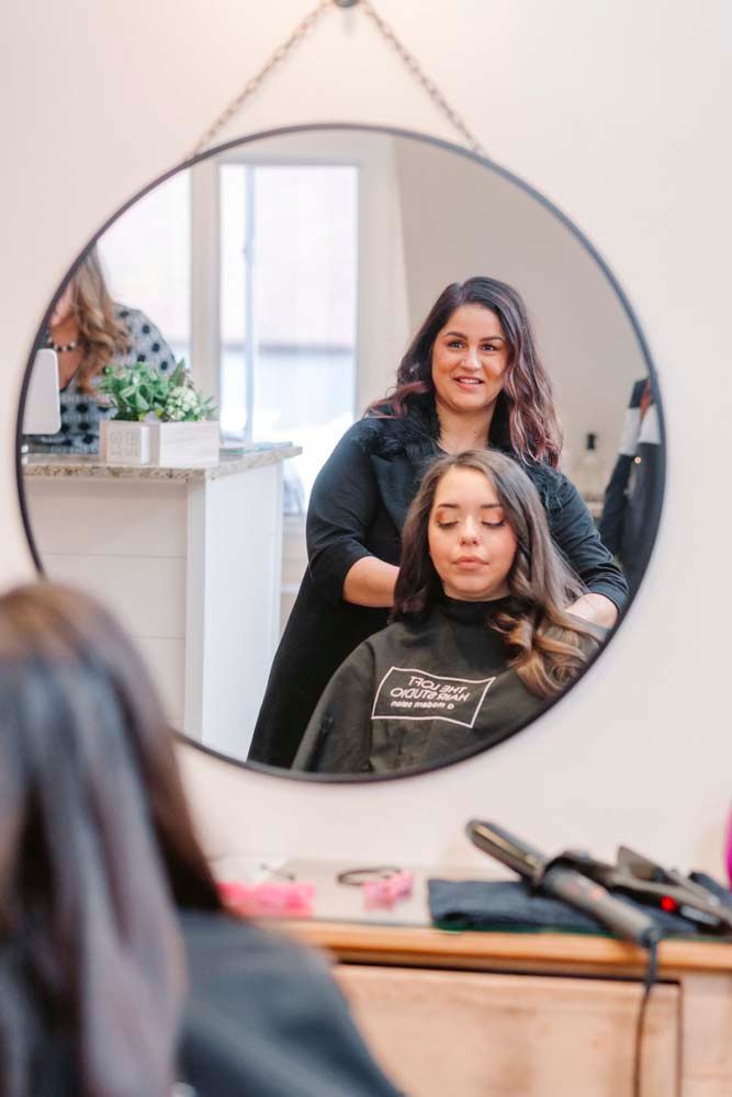 A woman is getting her hair cut by a hairdresser in front of a mirror.
