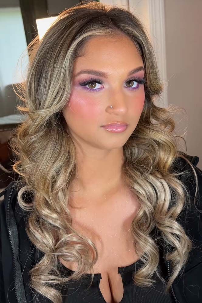 A woman with long blonde hair and purple eyeshadow is wearing a black top.