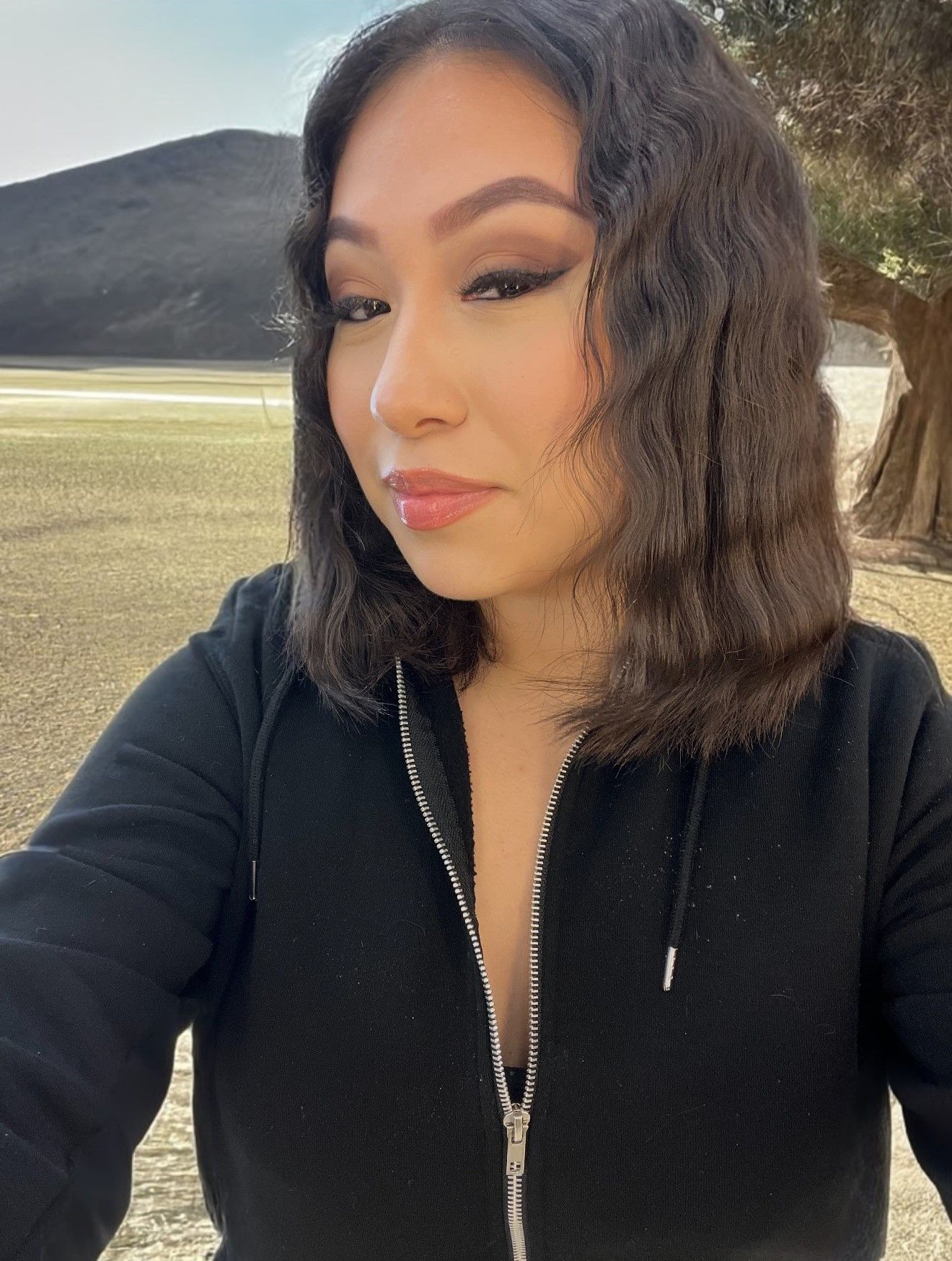 A woman in a black hoodie is taking a selfie.