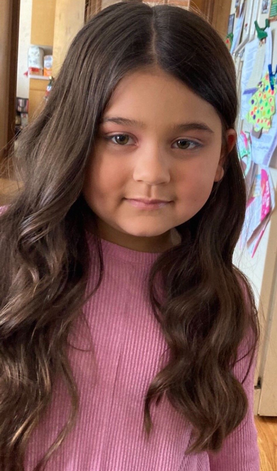 A little girl with long brown hair is wearing a pink sweater.