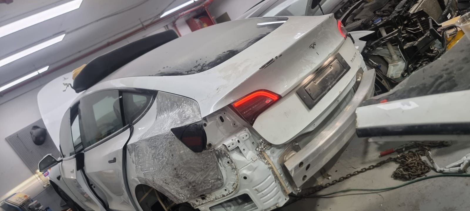 White Tesla car in a repair shop with rear damage and exposed metal panels.