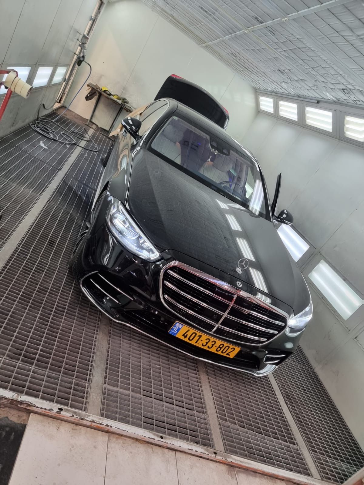 Black Mercedes-Benz sedan in a paint booth. Open door, grill and headlights visible.