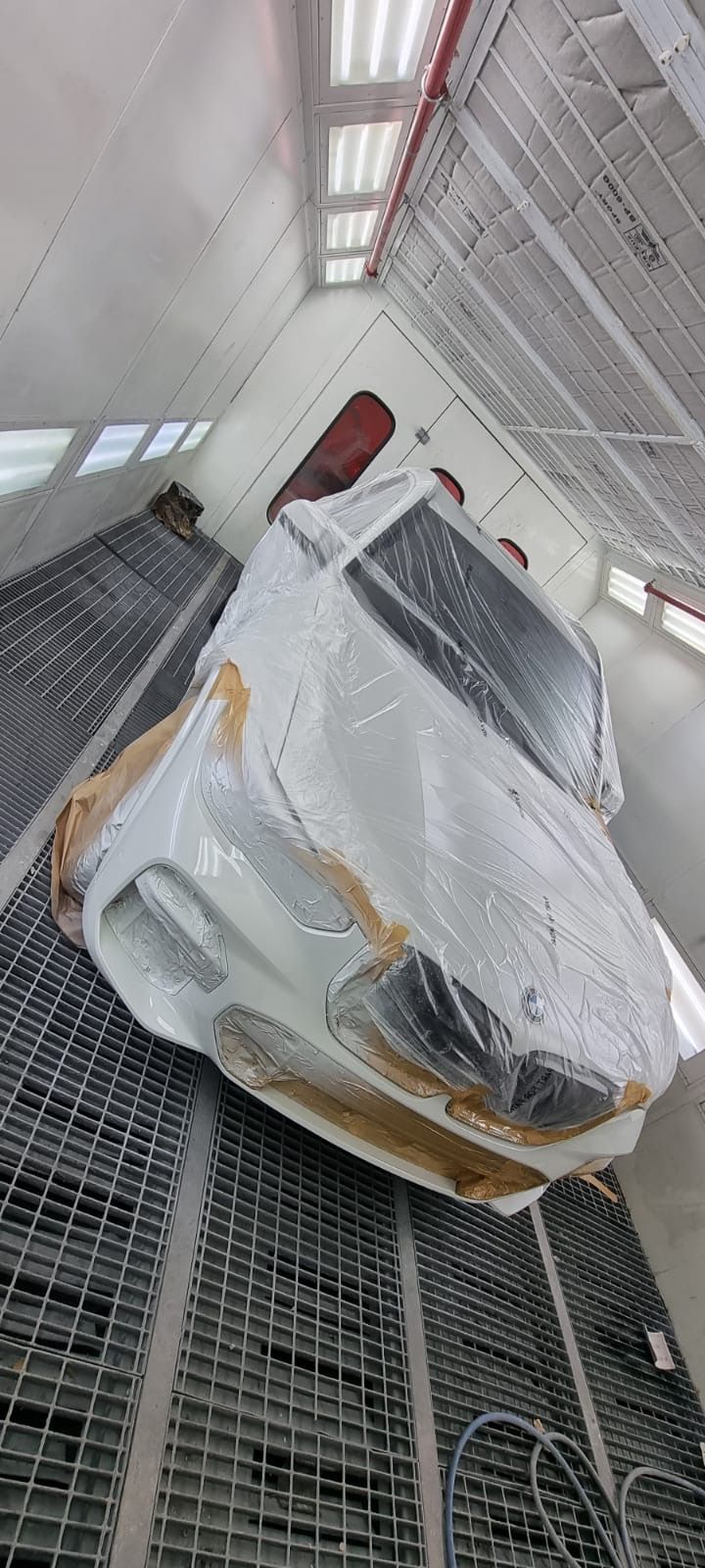 White car wrapped in plastic inside a paint booth.
