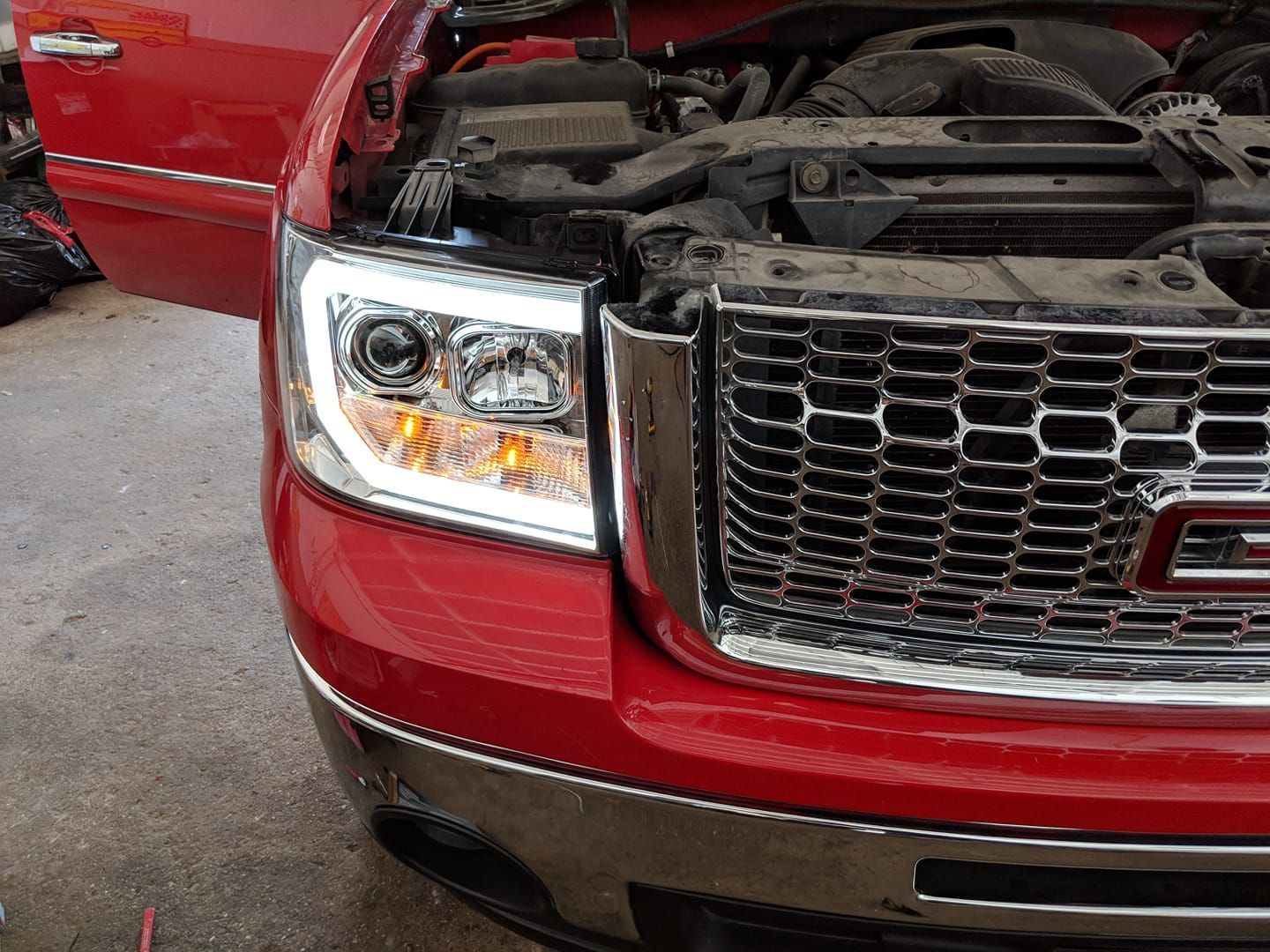 A red gmc truck with the hood open and the headlights on
