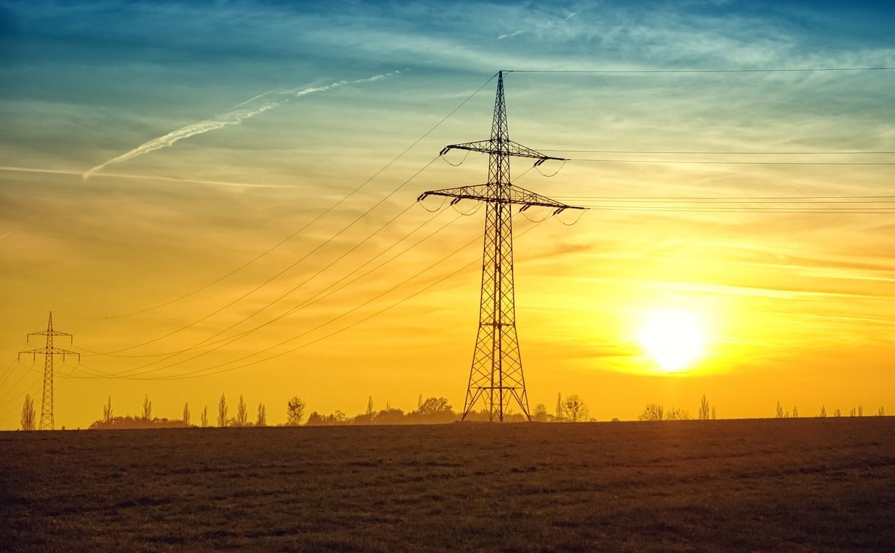 Una puesta de sol sobre un campo con líneas eléctricas en primer plano.