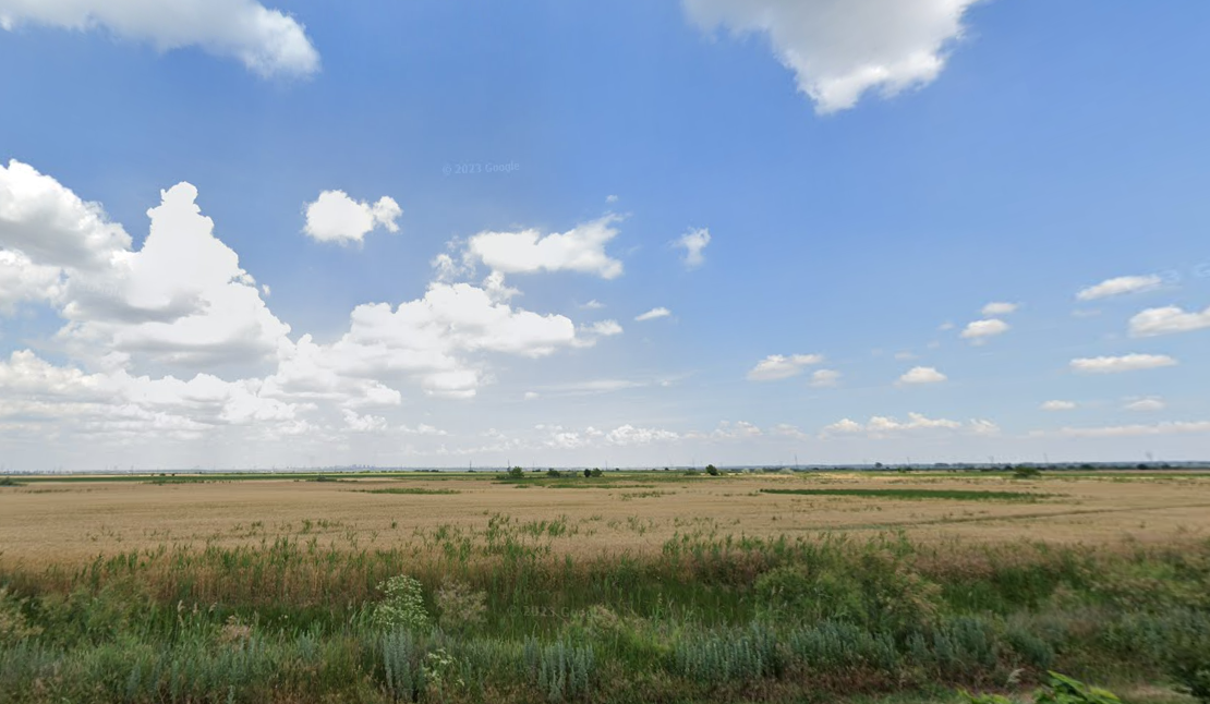 Un campo con un cielo azul y nubes blancas al fondo.