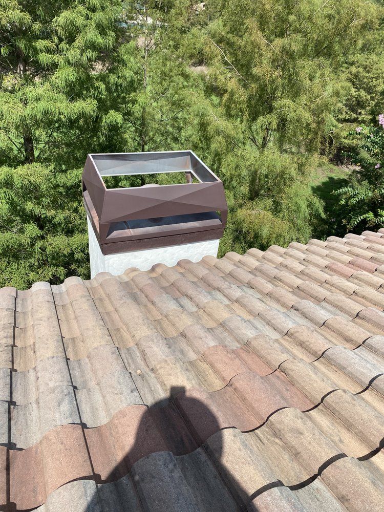 A chimney on top of a tiled roof with trees in the background.