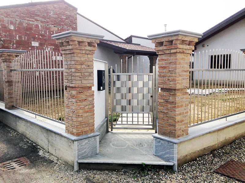 Una recinzione in mattoni con un cancello di metallo davanti a una casa