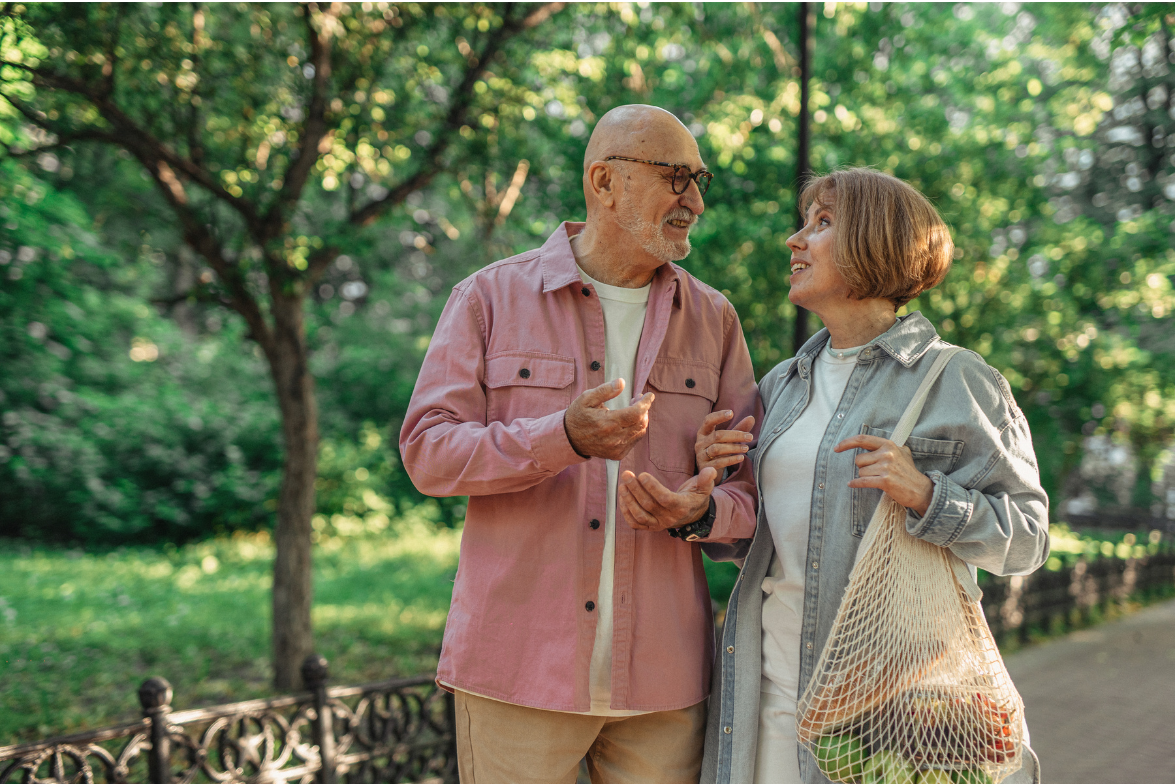 An elderly couple is walking in a park and talking to each other.