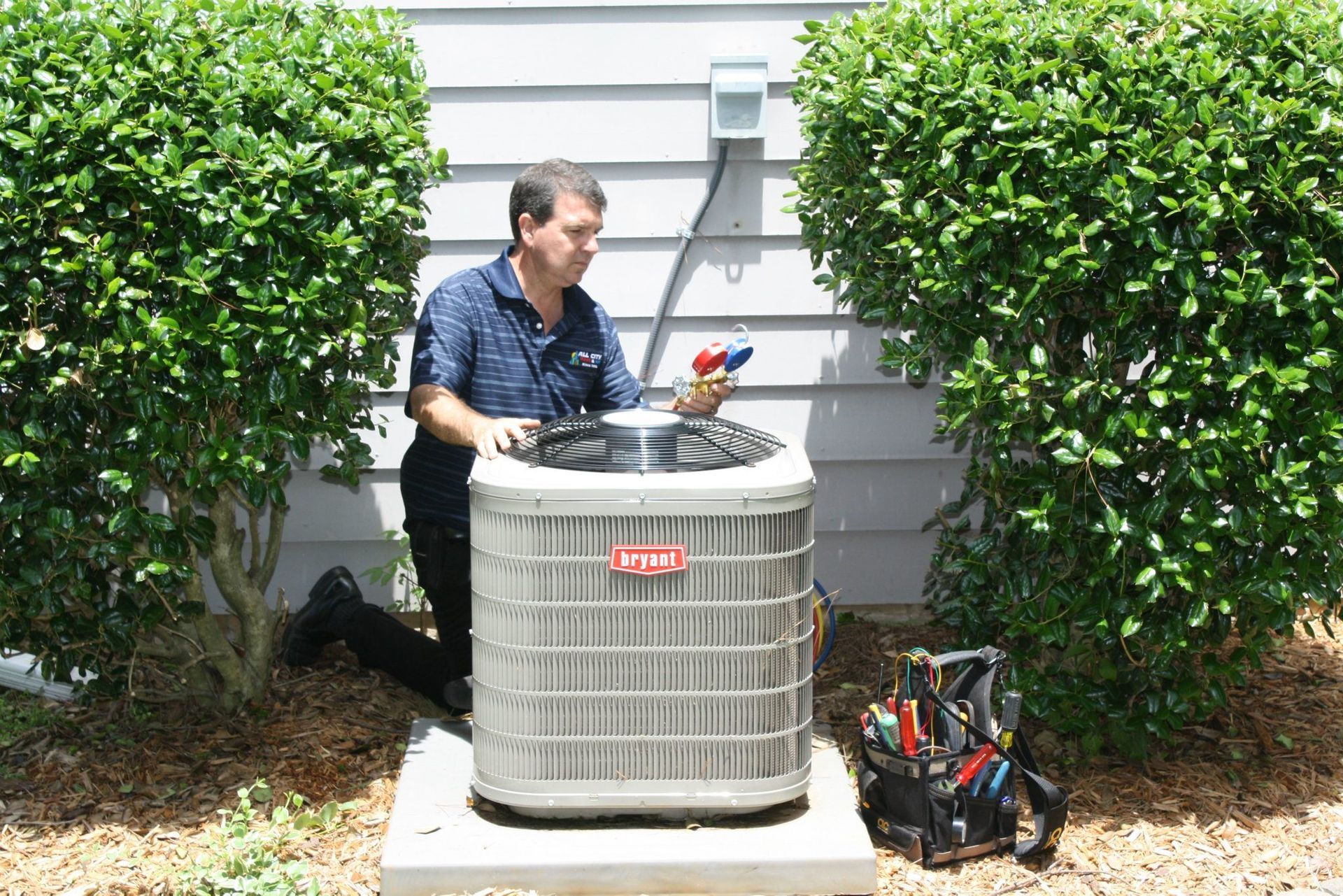 All City Heat and Air technician is working on an air conditioner outside of a house .