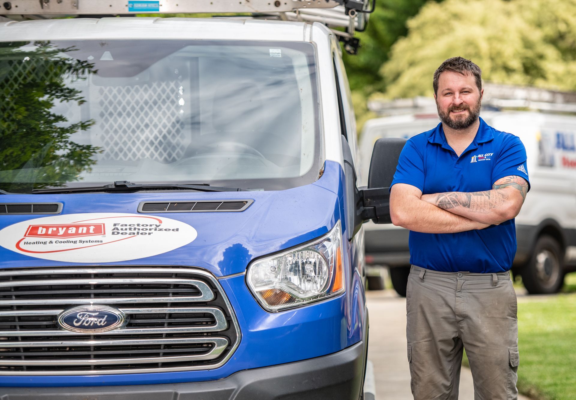 An All City Heat and Air technician is standing in front of an All City Heat and Air van with his arms crossed.