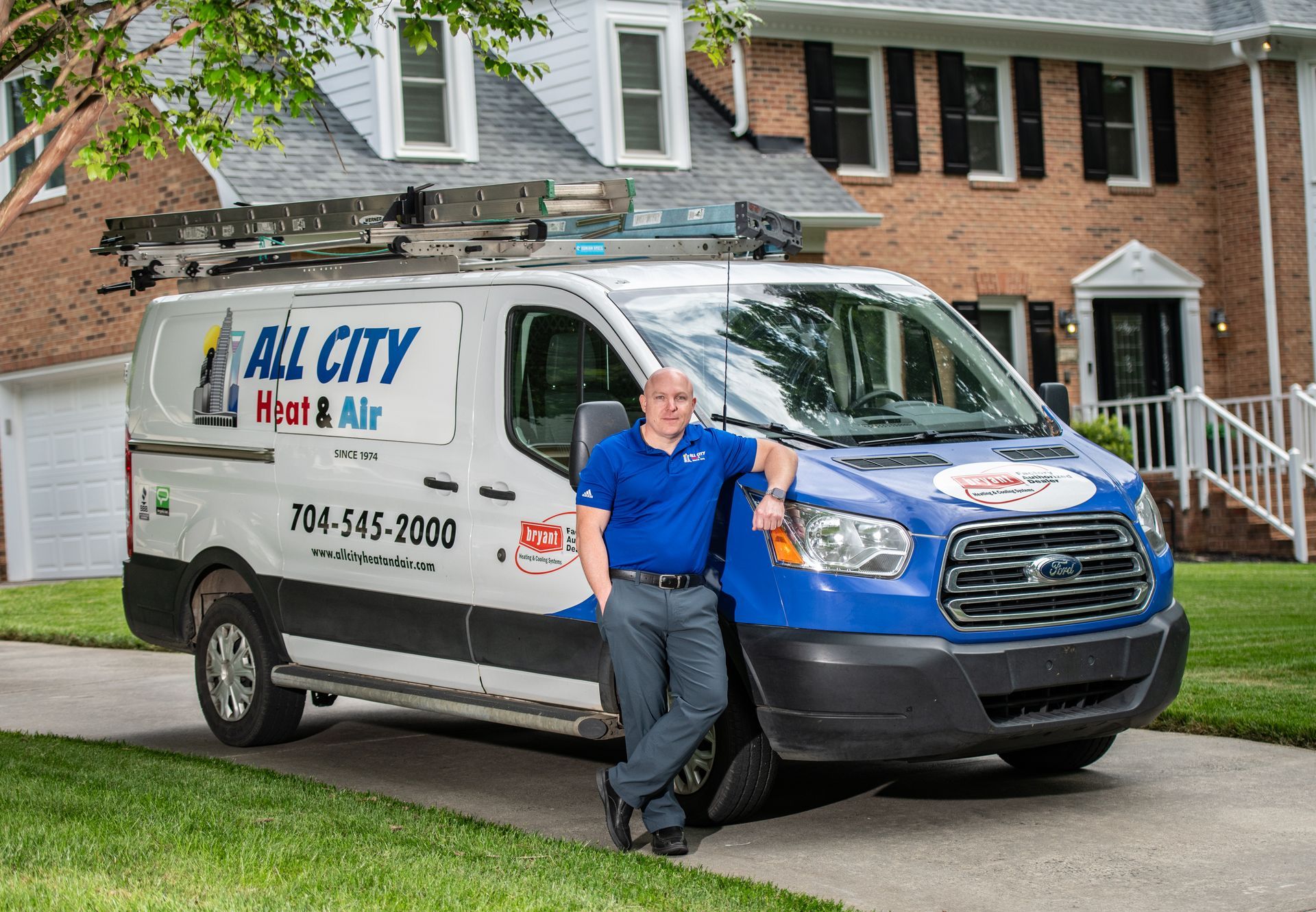 An All City Heat and Air technician is standing in front of an All City Heat and Air van in front of home.