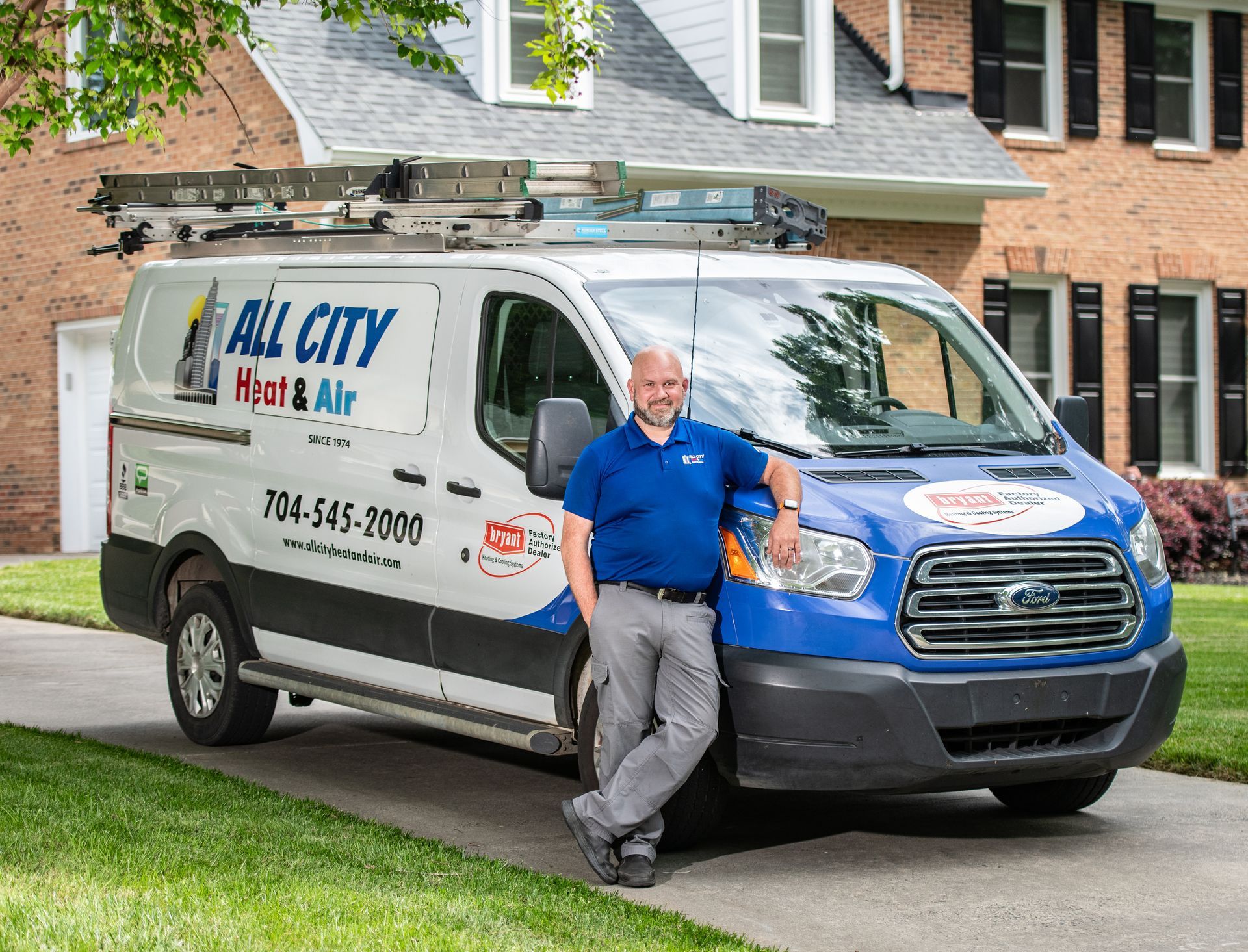 An All City Heat and Air technician is standing next to a van in front of a house.
