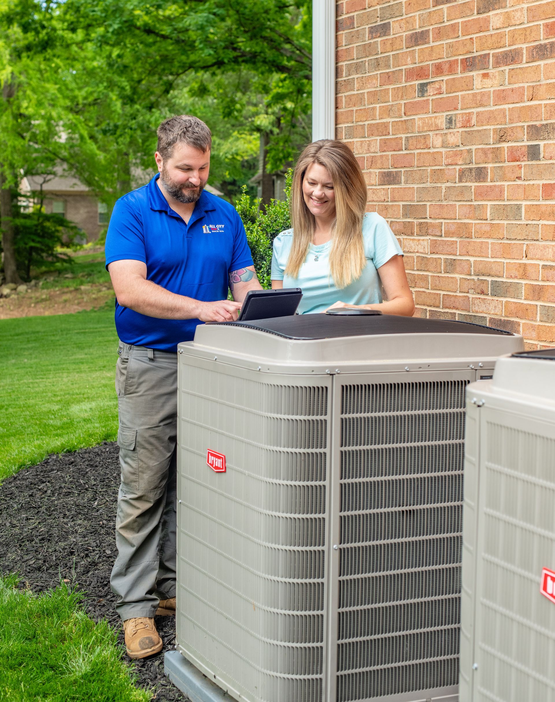 An All City Heat and Air technician and a woman are standing next to an air conditioner.