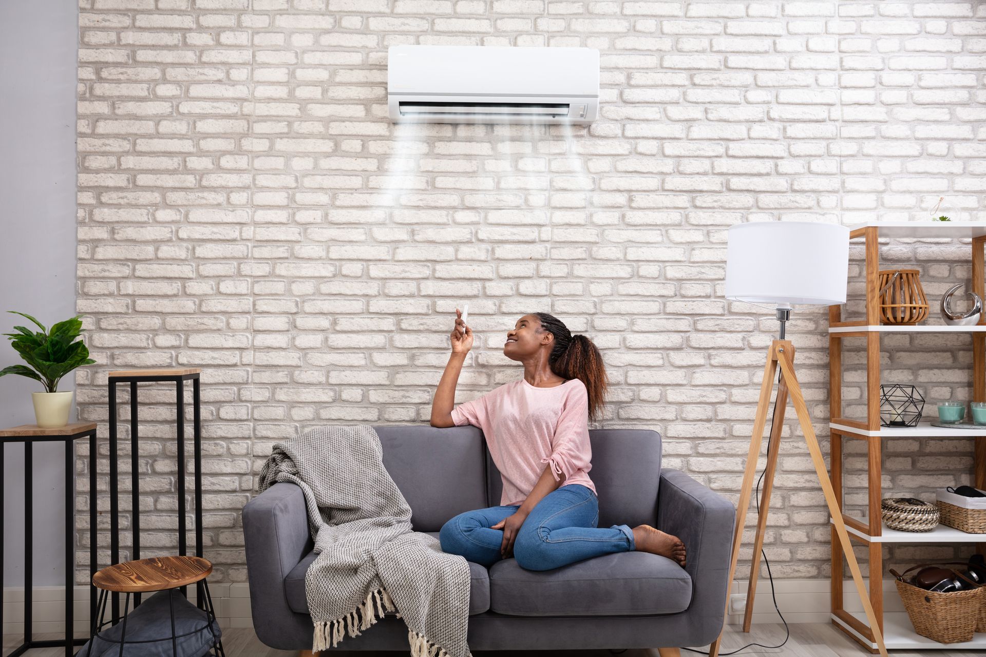 Woman on couch working her air conditioning unit with remote control.