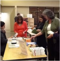 A group of people are standing around a table with books on it.