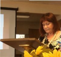 A woman is standing at a podium holding a bouquet of sunflowers.
