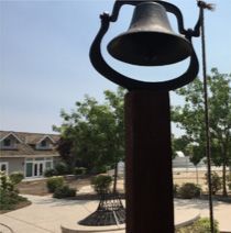 A bell is sitting on top of a wooden pole in a park.