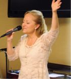 A woman is singing into a microphone with her arms in the air.