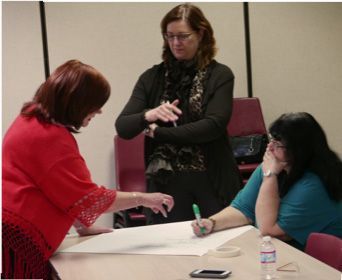 Three women are sitting at a table and one is writing on a piece of paper
